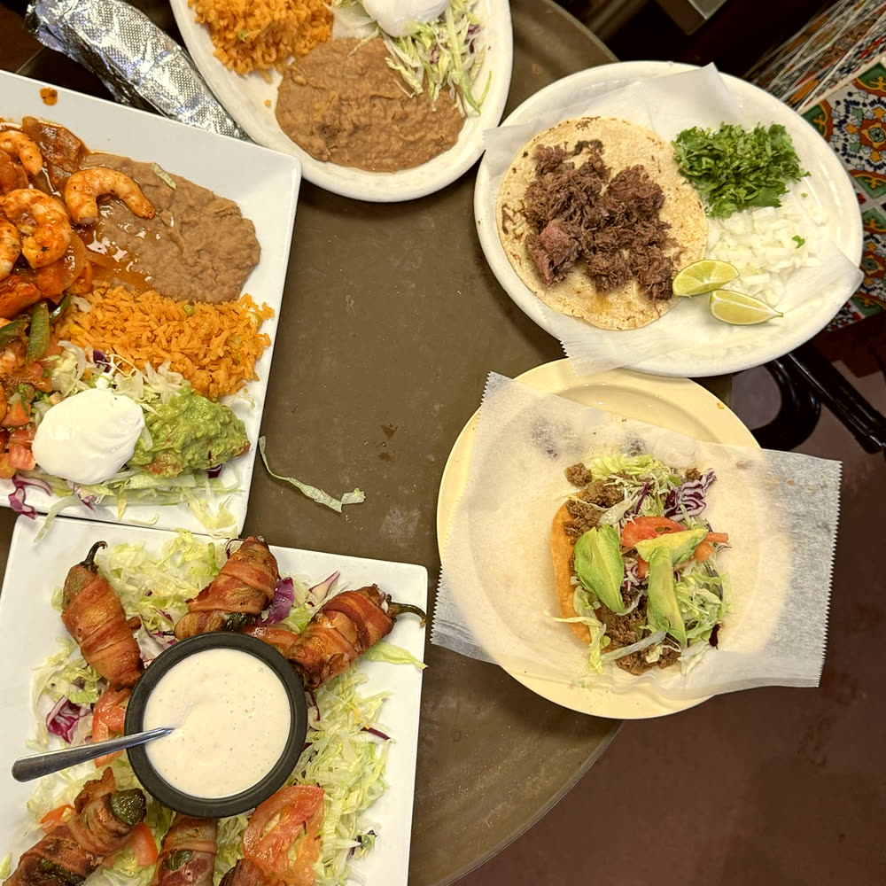 Shrimp plate with rice, refried beans and guacamole, beside a shredded beef taco, a tostada and bacon-wrapped jalapeños.