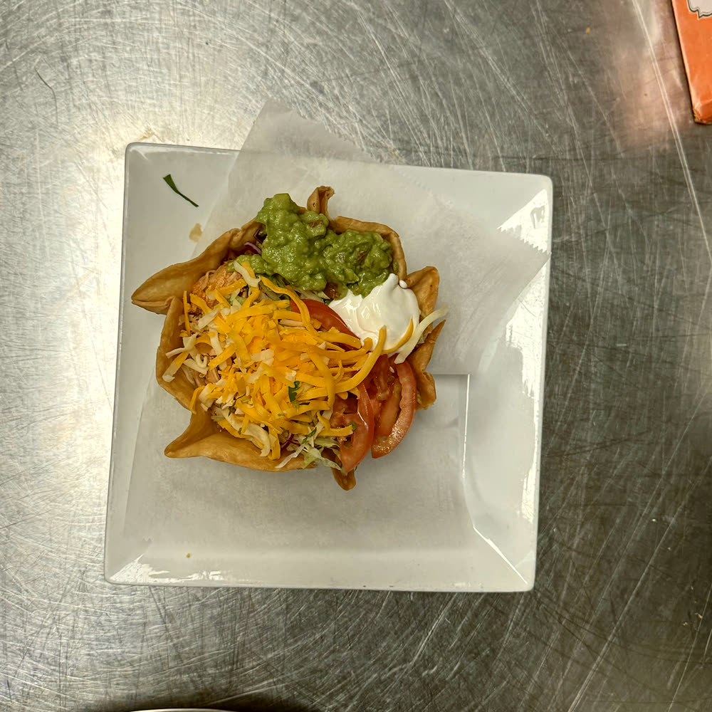 Taco salad in a crispy tortilla bowl with guacamole, sour cream, cheese and tomato.