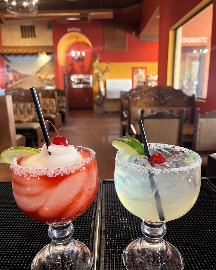 A strawberry margarita and a lime margarita, both salt rimmed, on the bar.