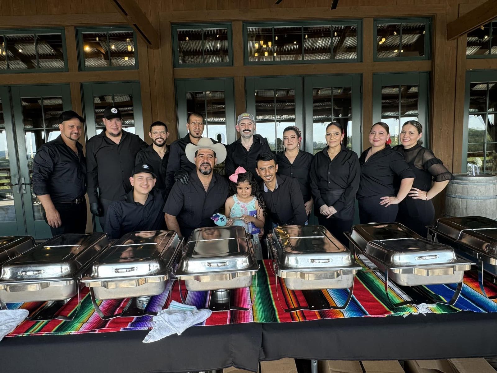 The staff of Tres Magueyes Cantina & Grill standing together behind a row of catering trays at an event.
